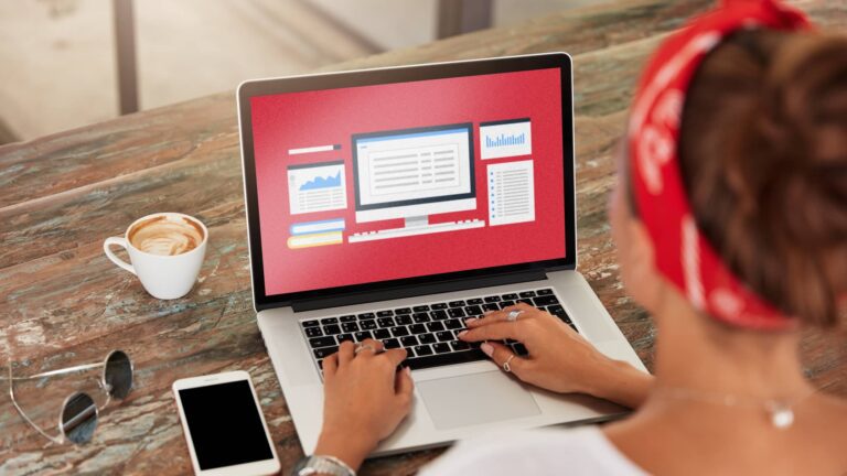 Person using a laptop with charts and graphs displayed on the screen, next to a smartphone and a cup of coffee on a wooden table.