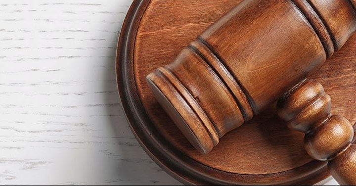 Close-up of a wooden judge’s gavel resting on a sound block on a white wooden surface.