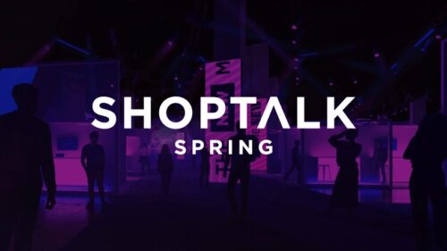 People walk in a dimly lit event space with purple lighting and the text “Shoptalk Spring” displayed prominently in the center.