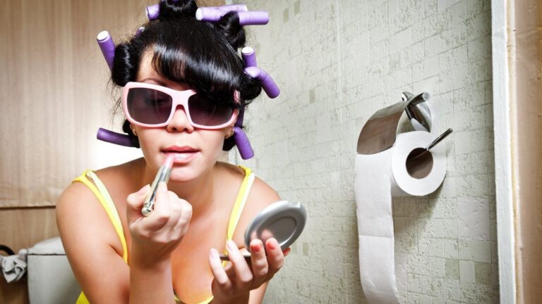 A woman in pink sunglasses putting on lipstick.