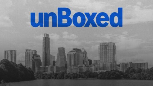 A grayscale city skyline with the word "unBoxed" in large blue letters centered at the top of the image.